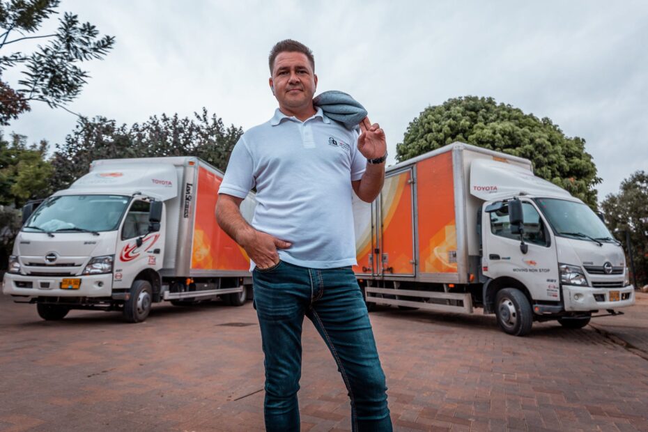 man in white polo shirt and denim jeans between delivery trucks